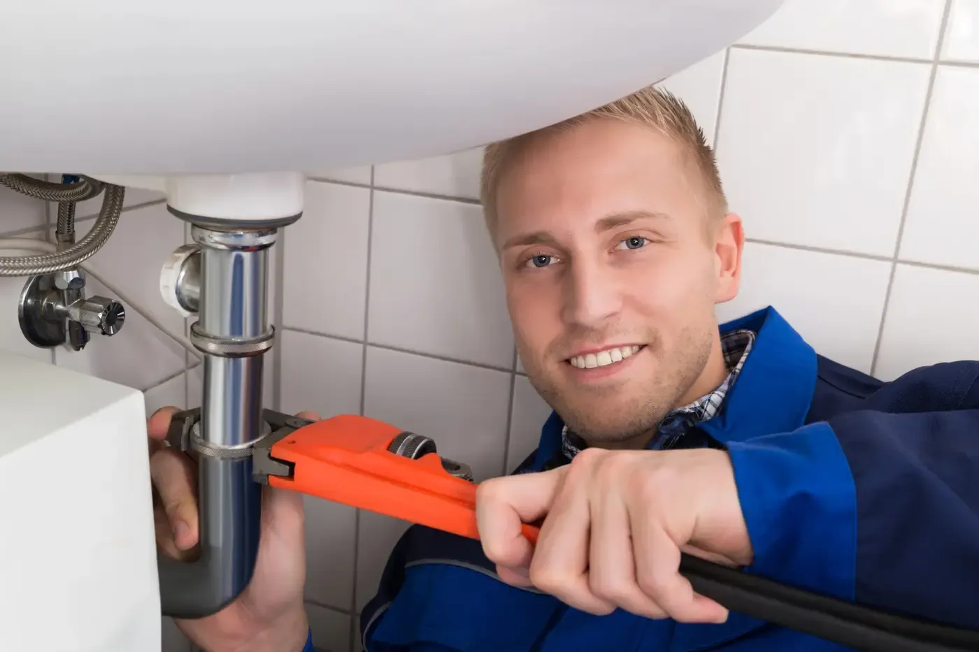 Plombier de l'équipe resserrant un siphon sous un lavabo à Évry-Courcouronnes